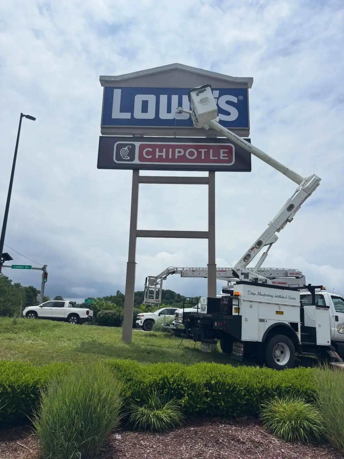 Signs Limited bucket truck servicing a Lowe's and Chipotle pylon sign